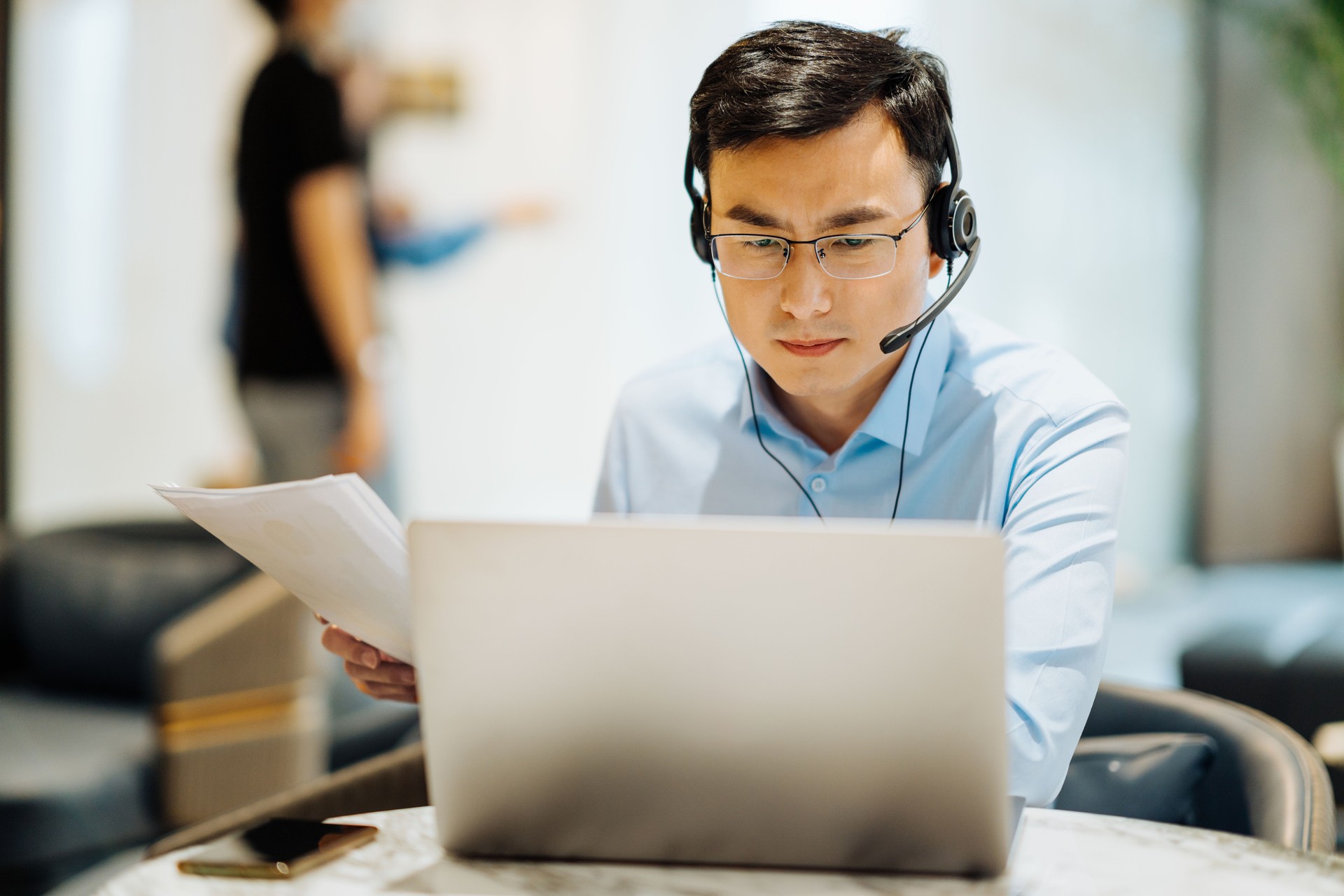 Asian businessman on videoconference with headset in modern office, capture the serious and contemplative emotions.